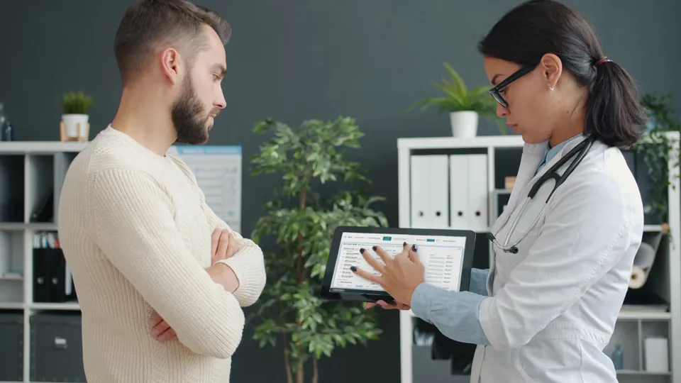 A clinician walks a patient through their results on a tablet showing the Cuneate dashboard.