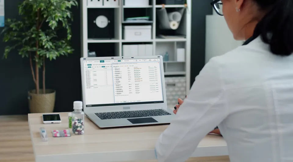 A clinician at a desk with the Cuneate dashboard open on a laptop: the caseload on the left, one patient's results on the right.
